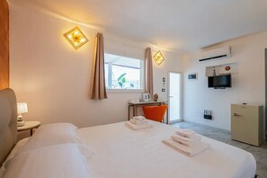 A hotel room with a bed, a desk, a chair, a TV, and a minibar.