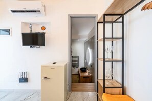 Een moderne kamer met een flatscreen televisie aan de muur, een klein kastje met een deur, een plank met glazen en een houten bankje.