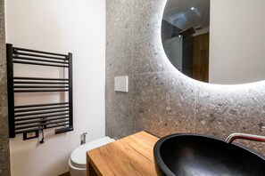 Un baño con toallero negro, tocador de madera, espejo redondo y váter blanco.