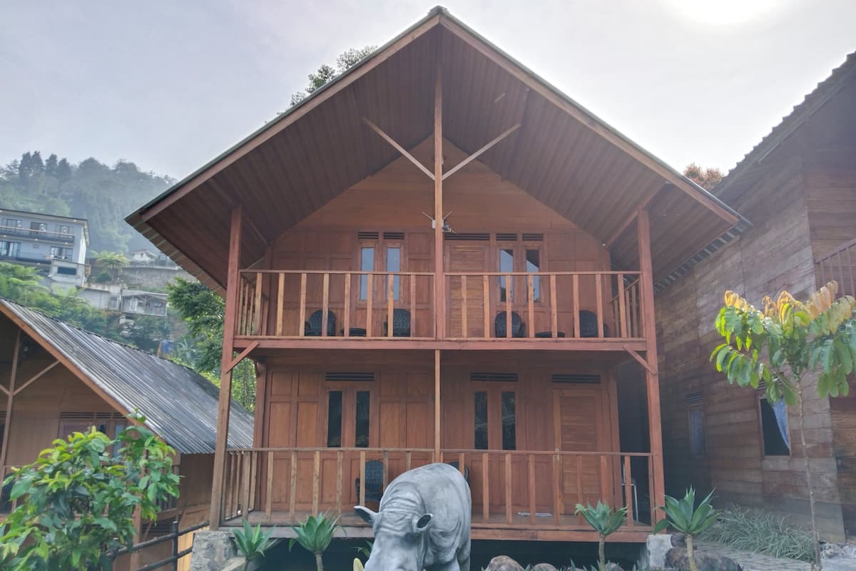 A two-story wooden building with a balcony, surrounded by a garden with rocks and plants.