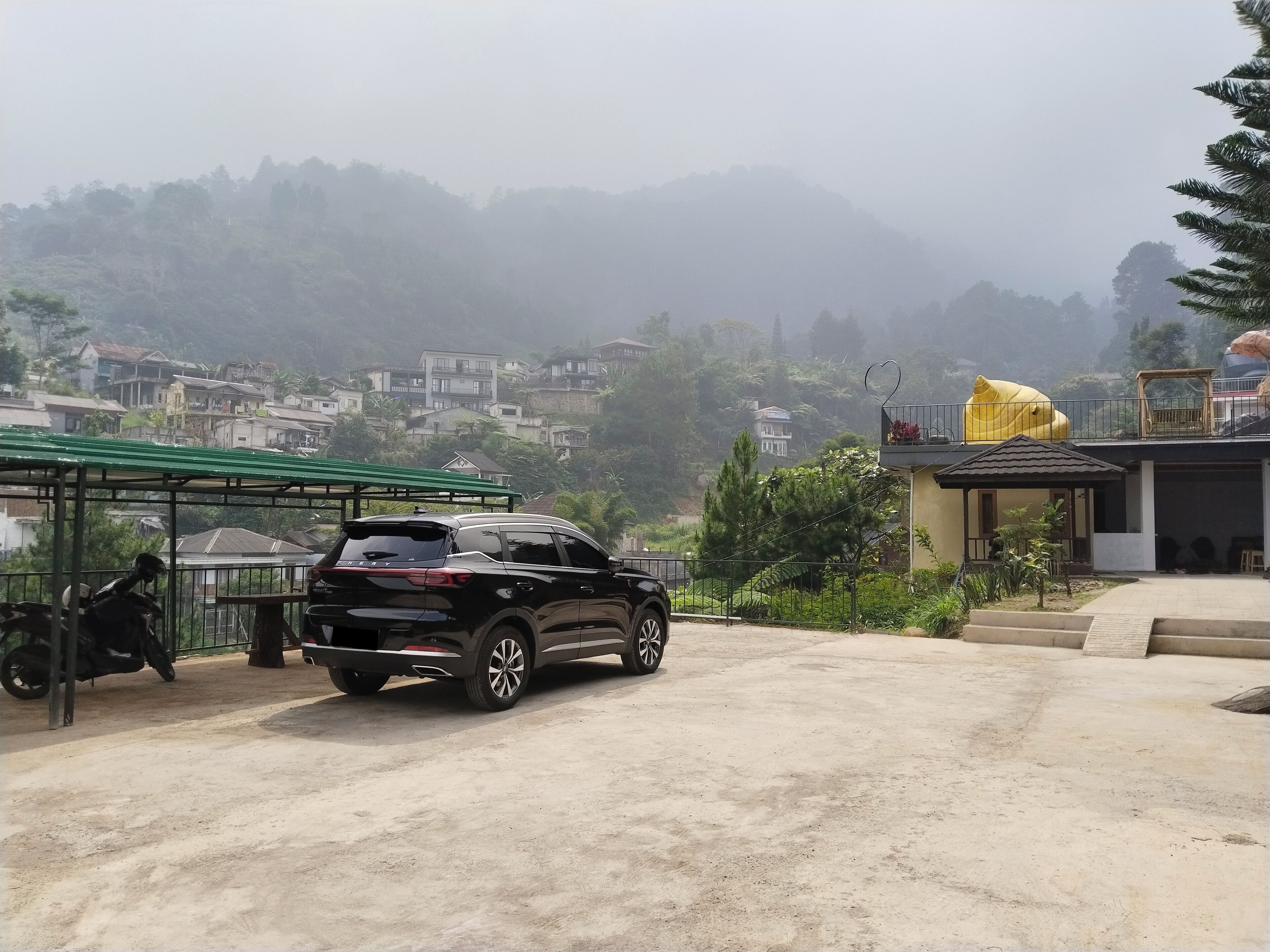 A black SUV parked in a covered area with a green roof, surrounded by a residential neighborhood with houses and trees.