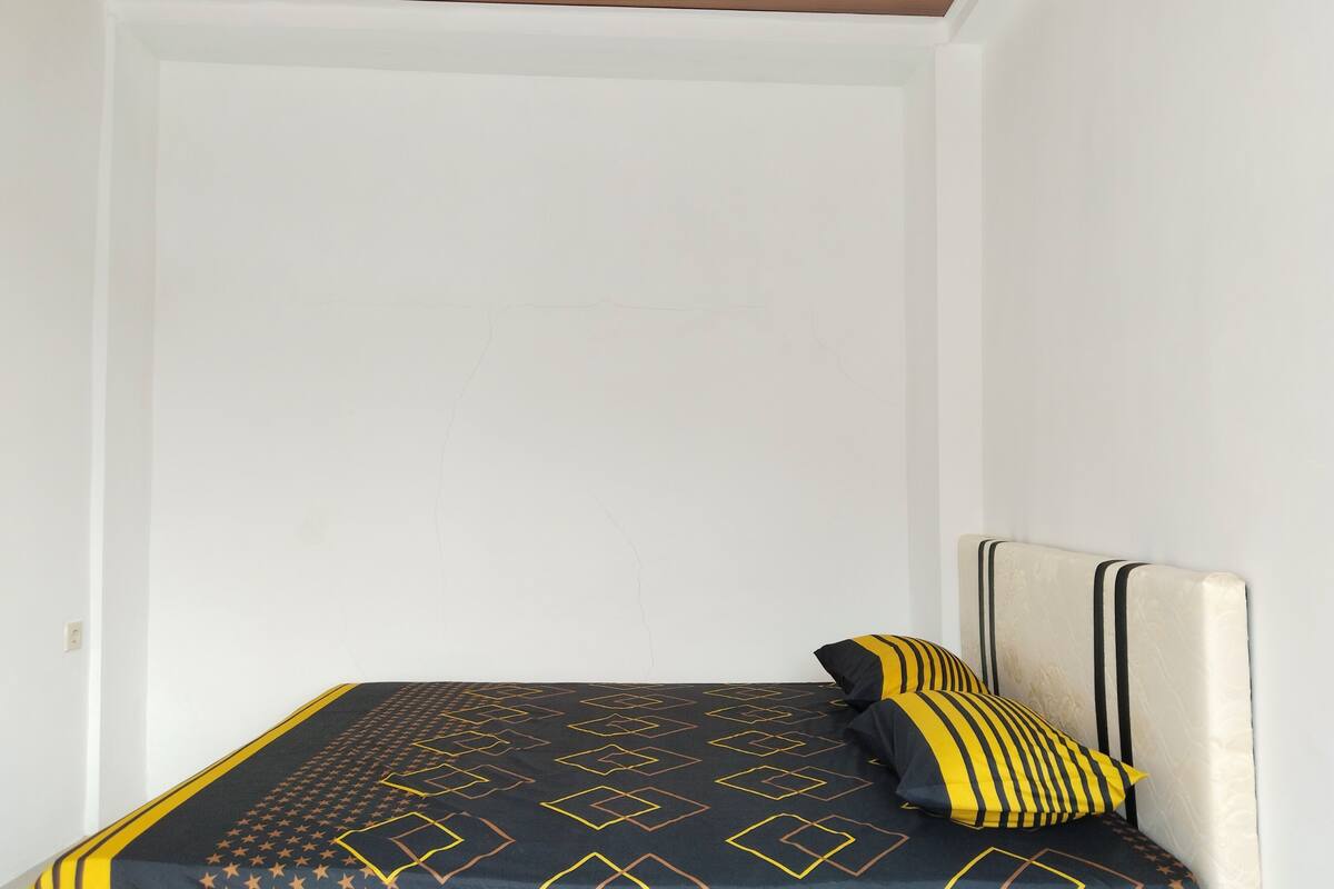 A bed with a geometric patterned bedspread and two pillows, one with stripes.
