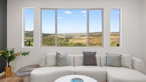 A modern living room with a large window, a sofa, and a small table. - @ Marbella Lane - Curated 5BR in Upscale RMV Haven (San Juan Capistrano)