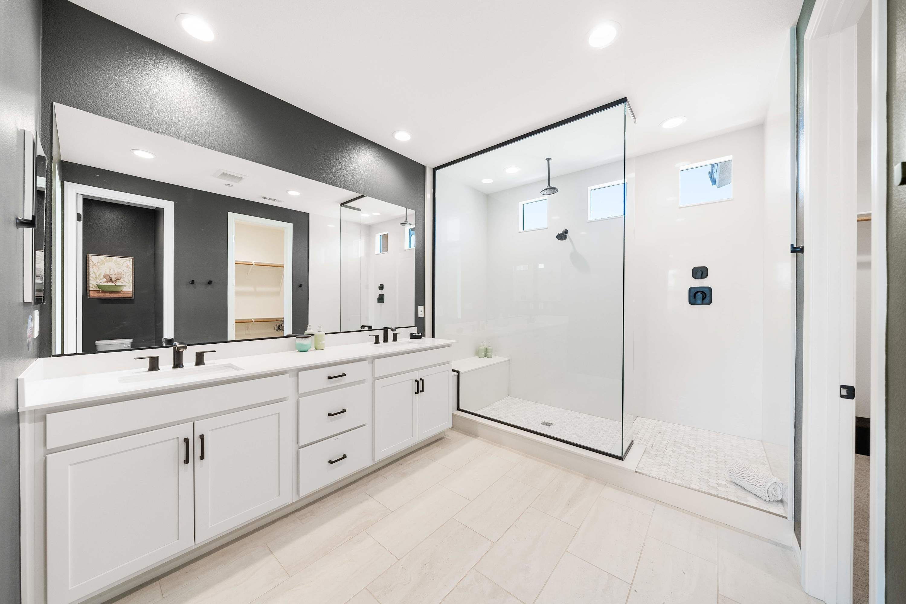 A modern bathroom with a large mirror, dual sinks, a walk-in shower, and a tiled floor.