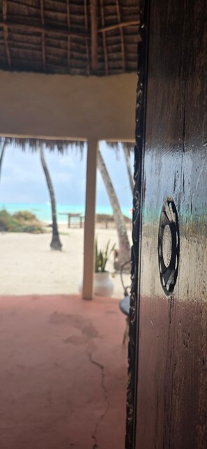 Une porte en bois dotée d’une poignée circulaire, qui donne sur une vue sur la plage, avec des palmiers et une plage de sable.