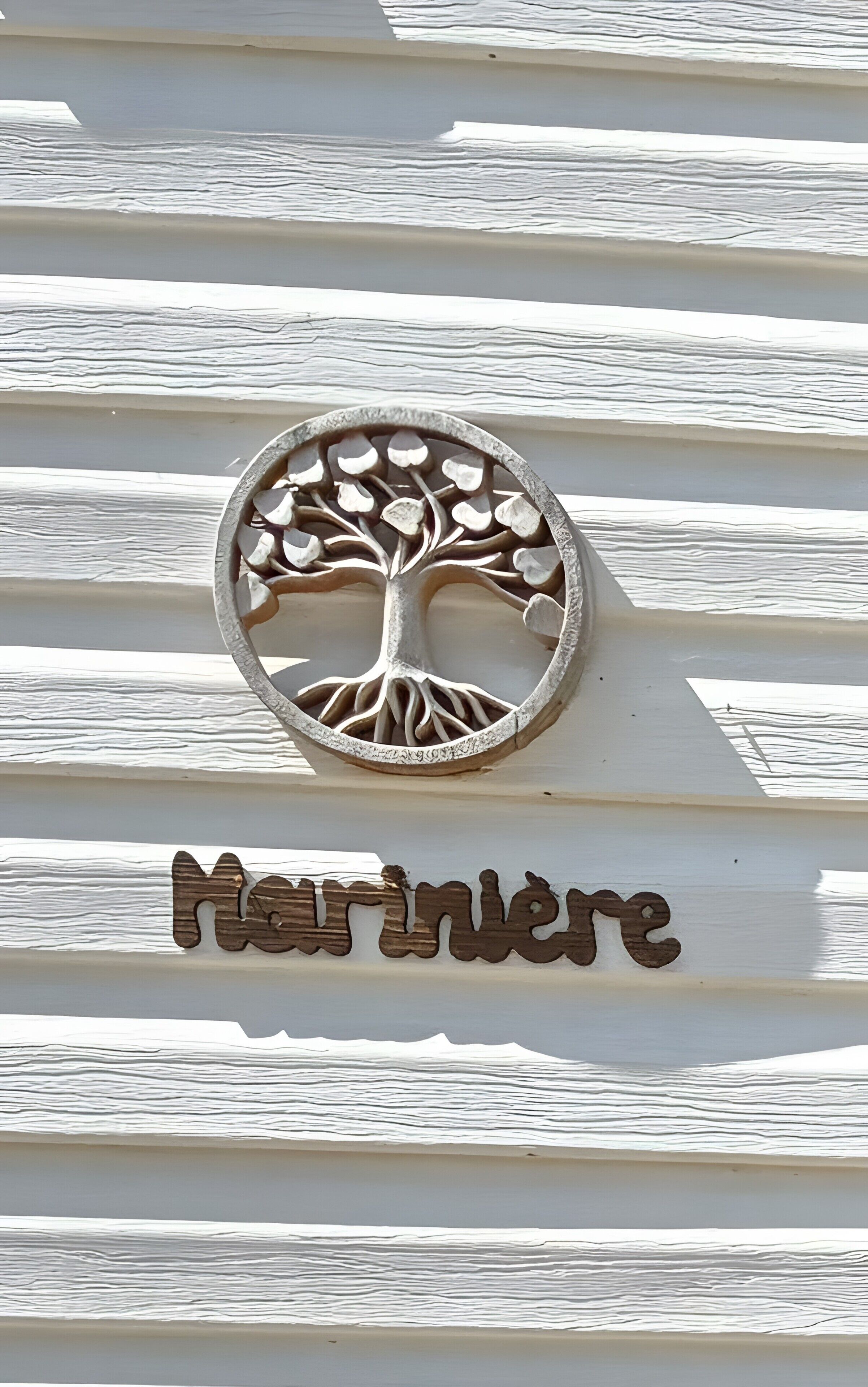 A tree-shaped metal plaque with the name 'Marinlère' on a white wooden wall.