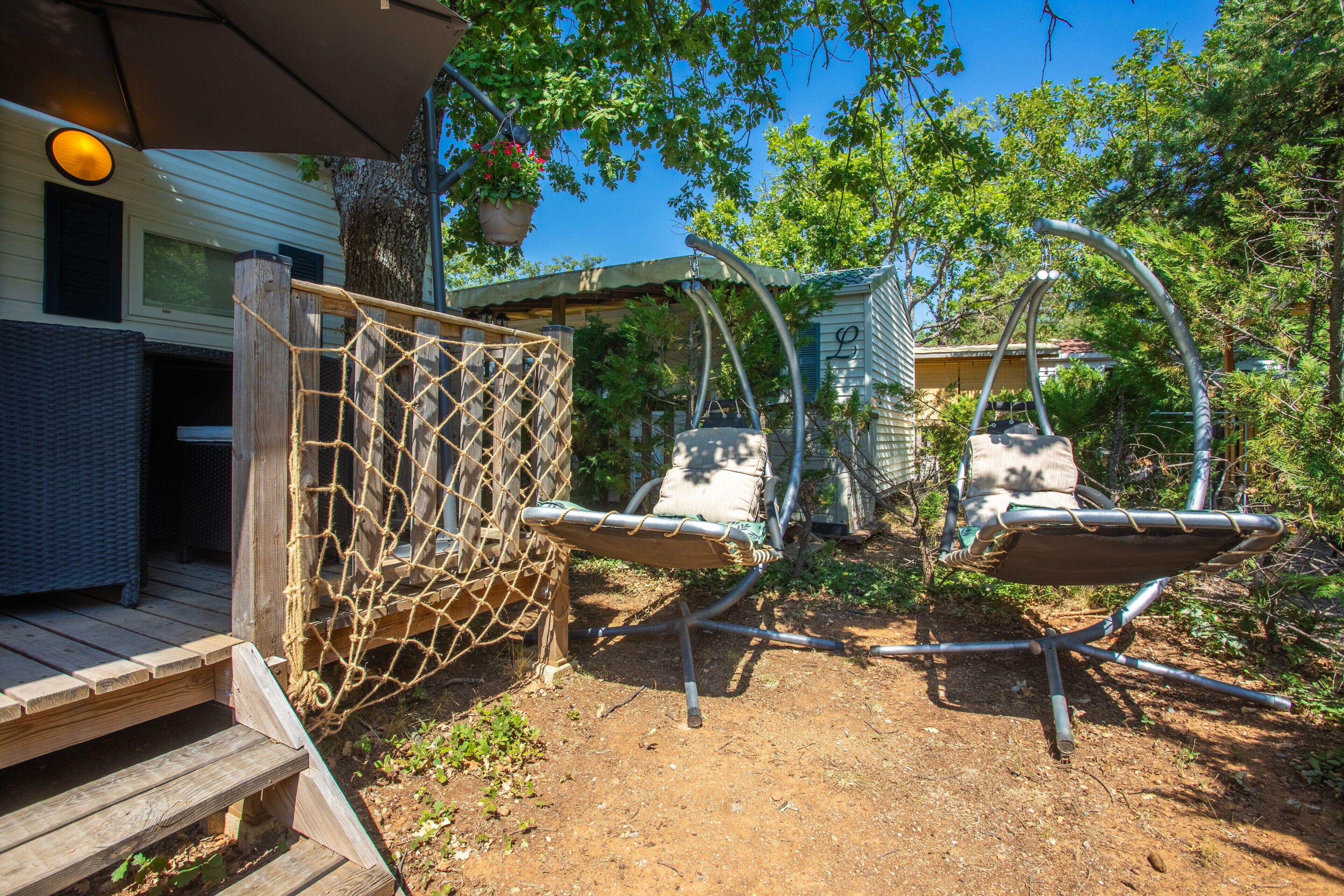 Une terrasse en bois avec un filet en corde, deux chaises suspendues et un petit espace salon abrité.