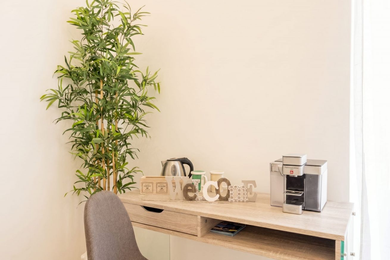 Un espace de travail comprenant un bureau, une machine à café, une plante et une pancarte « Bienvenue ».