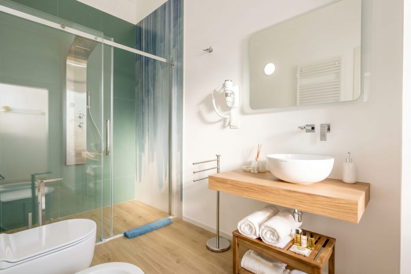 A modern bathroom with a glass-enclosed shower, a freestanding toilet, a large mirror, and a wooden vanity with a white sink.