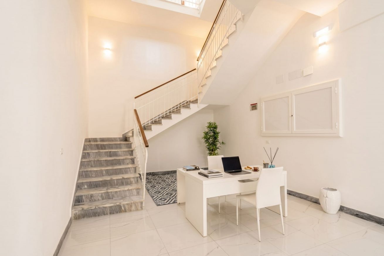 A modern interior with a staircase, a desk with a laptop, and a potted plant.