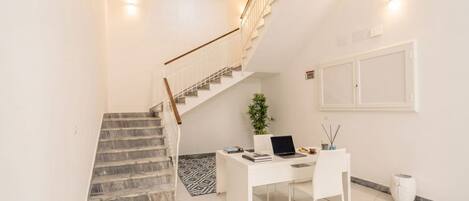 A modern interior with a staircase, a desk with a laptop, and a potted plant.