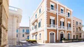 A multi-story building with balconies, a prominent entrance, and a clear sky. - Simona - Italian Living (Monopoli)