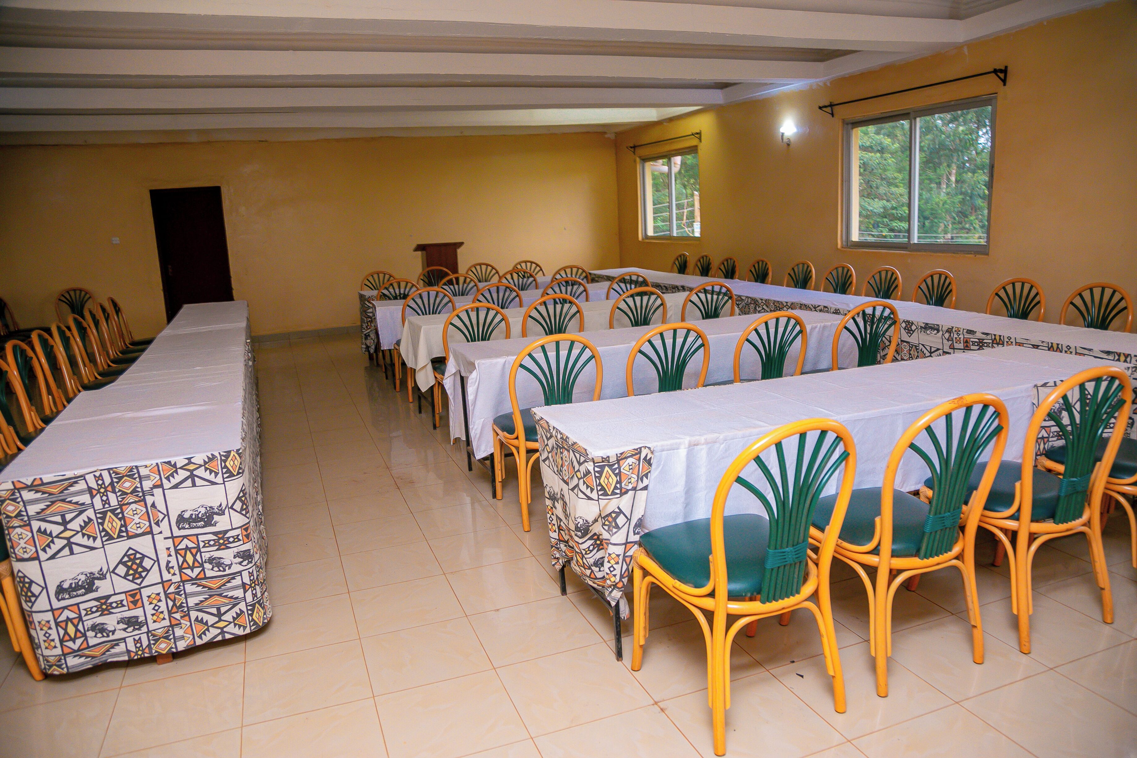 A conference room with a long table and chairs, a podium, and a window with a view of trees.