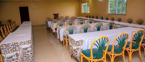 A conference room with a long table and chairs, a podium, and a window with a view of trees.