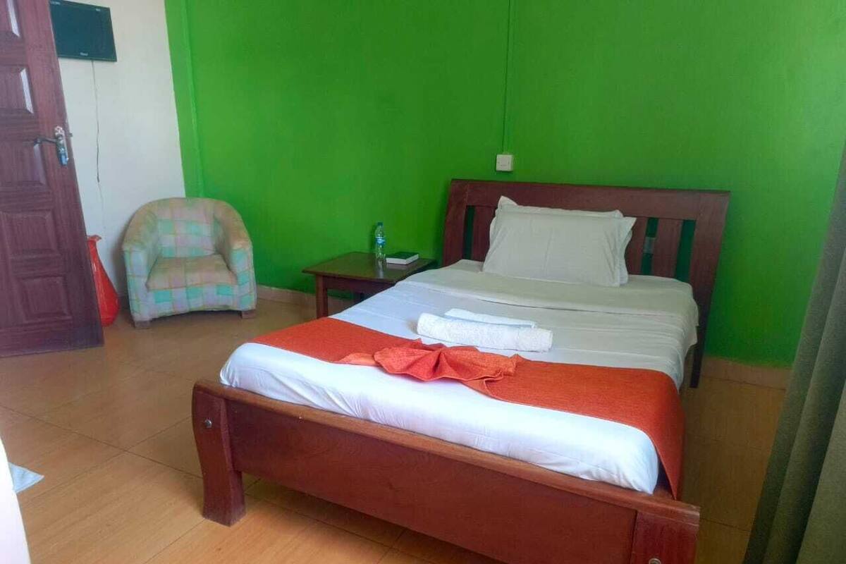 A room with a wooden bed, a nightstand, a chair, and a green wall.