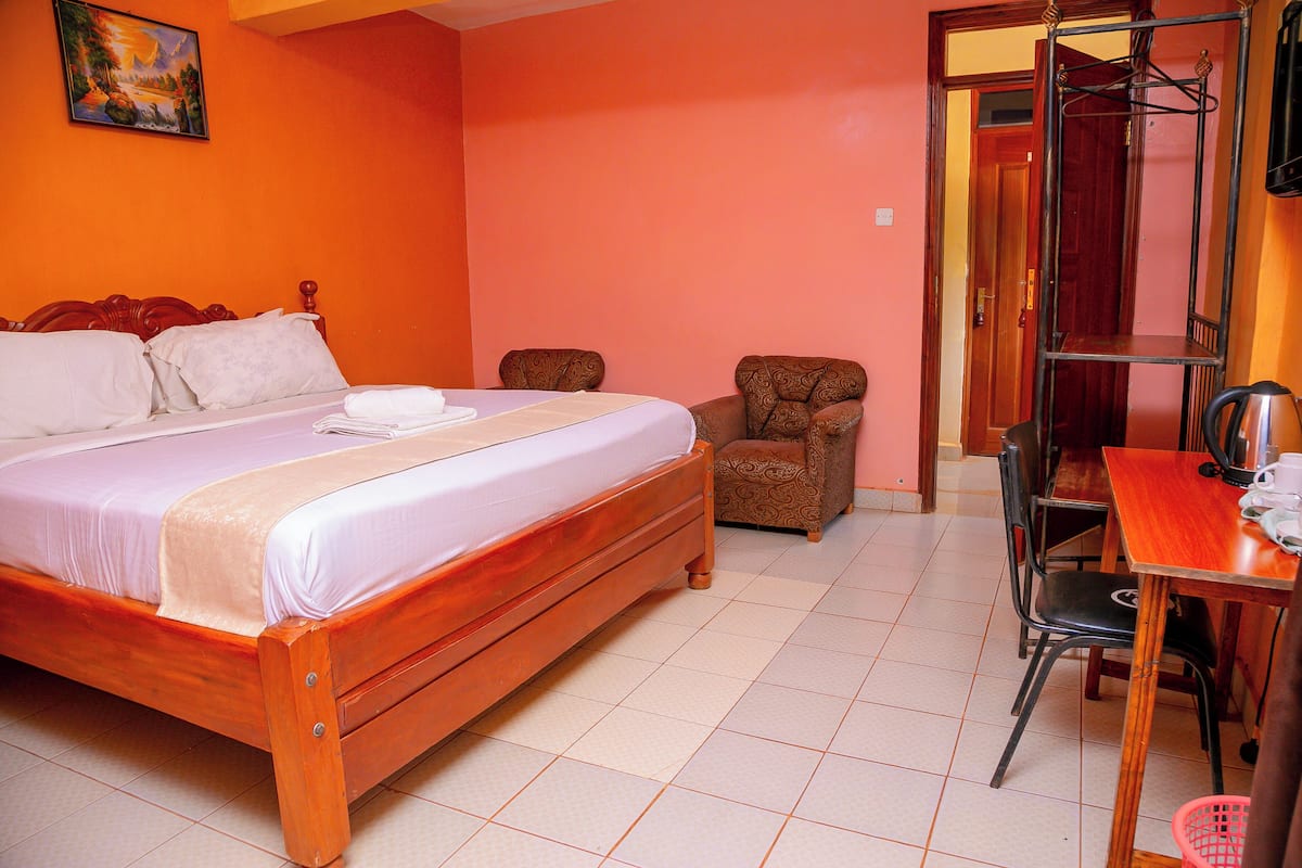 A bedroom with a wooden bed, a chair, a table, and a shelf.