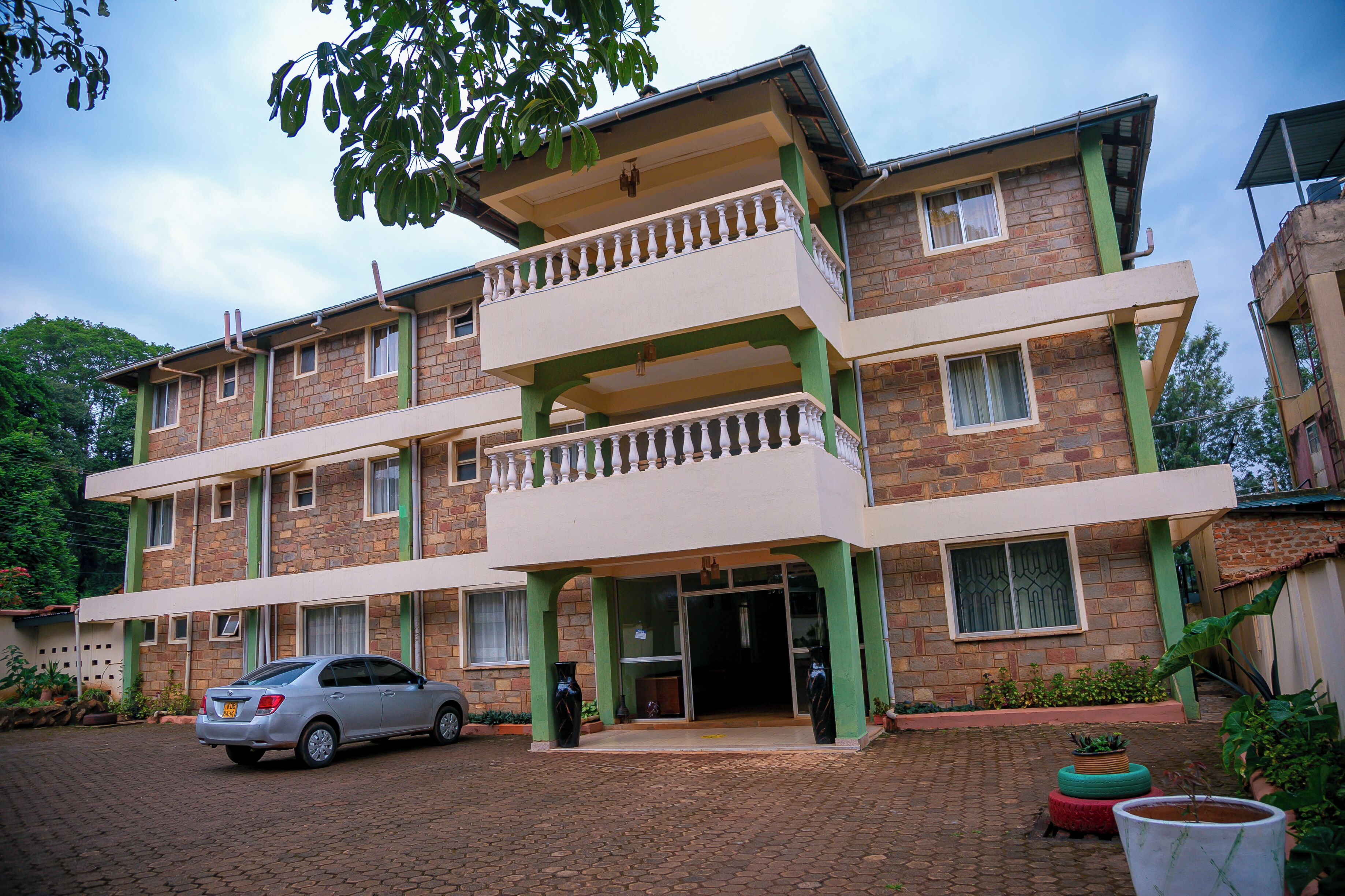 A multi-story building with a brick facade, green balconies, and a car parked in front.