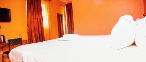 A hotel room with a bed, a desk, a chair, and a television on the wall.