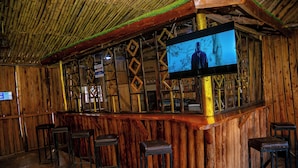 Zona de bar rústica amb parets de fusta, sostre de bambú i un televisor de pantalla plana penjat a la paret.