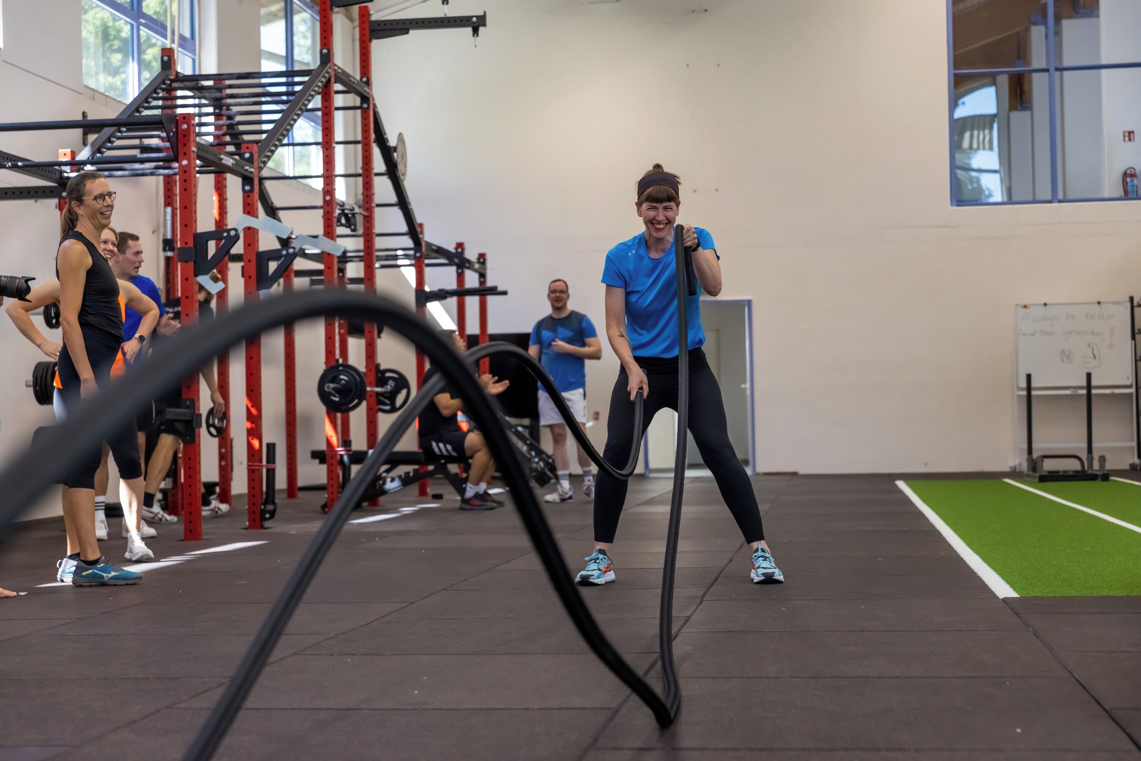 Un gimnasio con equipo de ejercicio, una pizarra y una zona de césped artificial verde.