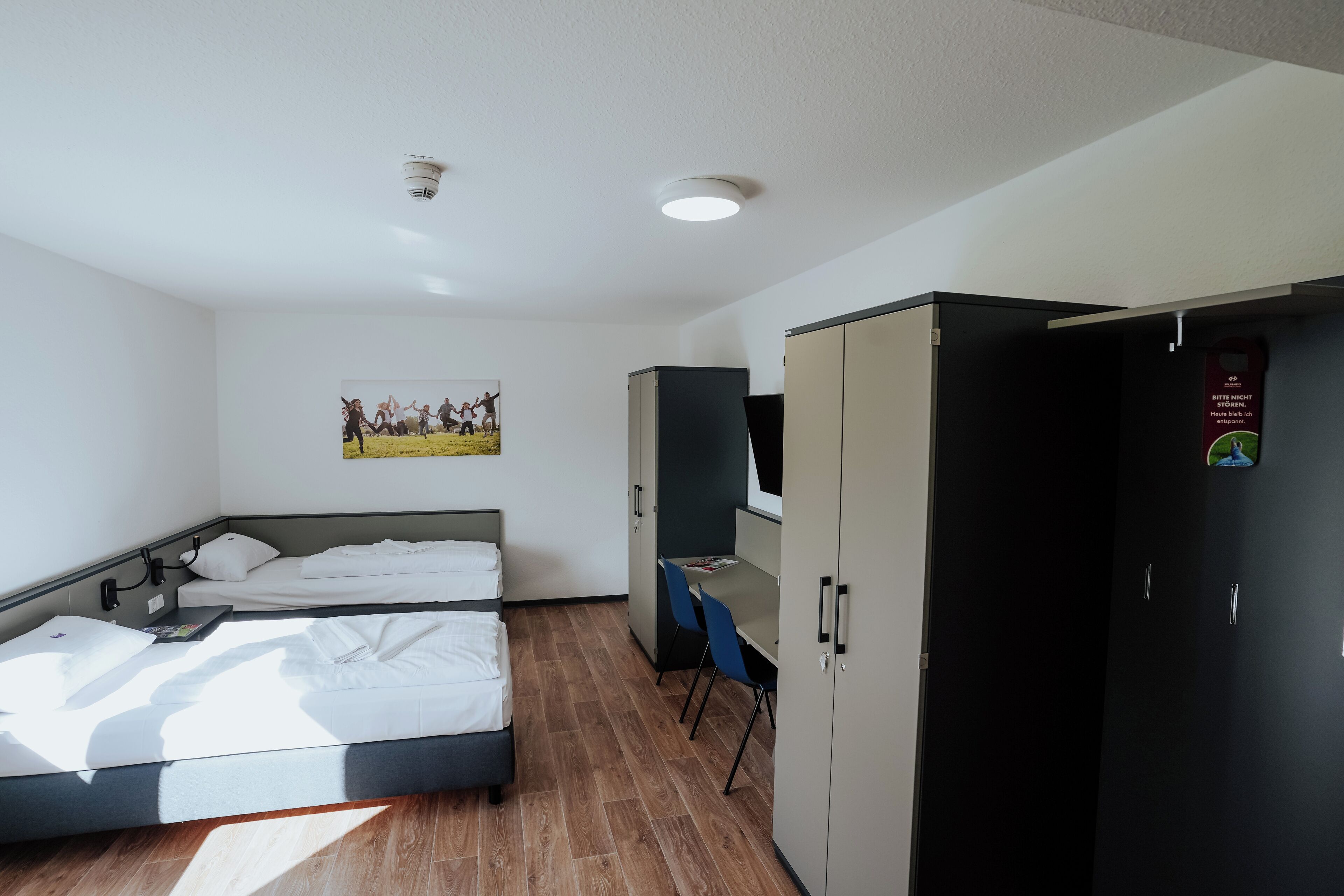 A hotel room with two beds, a wardrobe, a desk, and a wall-mounted picture.
