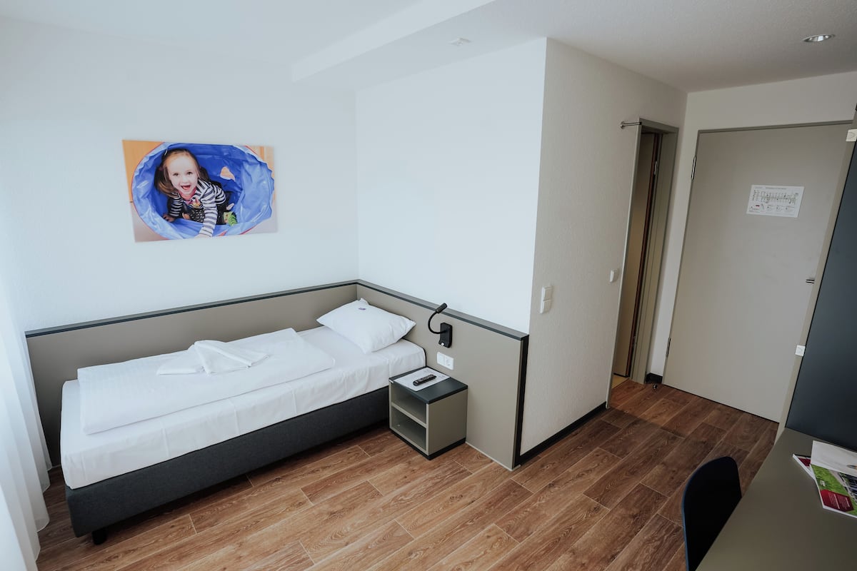 Un dormitorio pequeño y ordenado con una cama individual, una mesita de noche y un cuadro colgado en la pared.