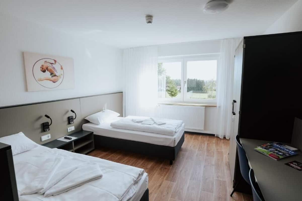 Una habitación de hotel con dos camas, un escritorio, un radiador y una ventana con cortinas.