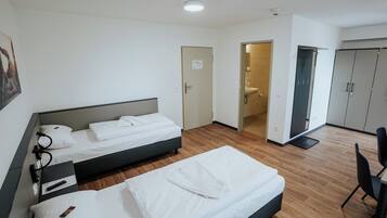 Une chambre d’hôtel avec deux lits, un bureau avec une chaise, une salle de bain et une armoire.