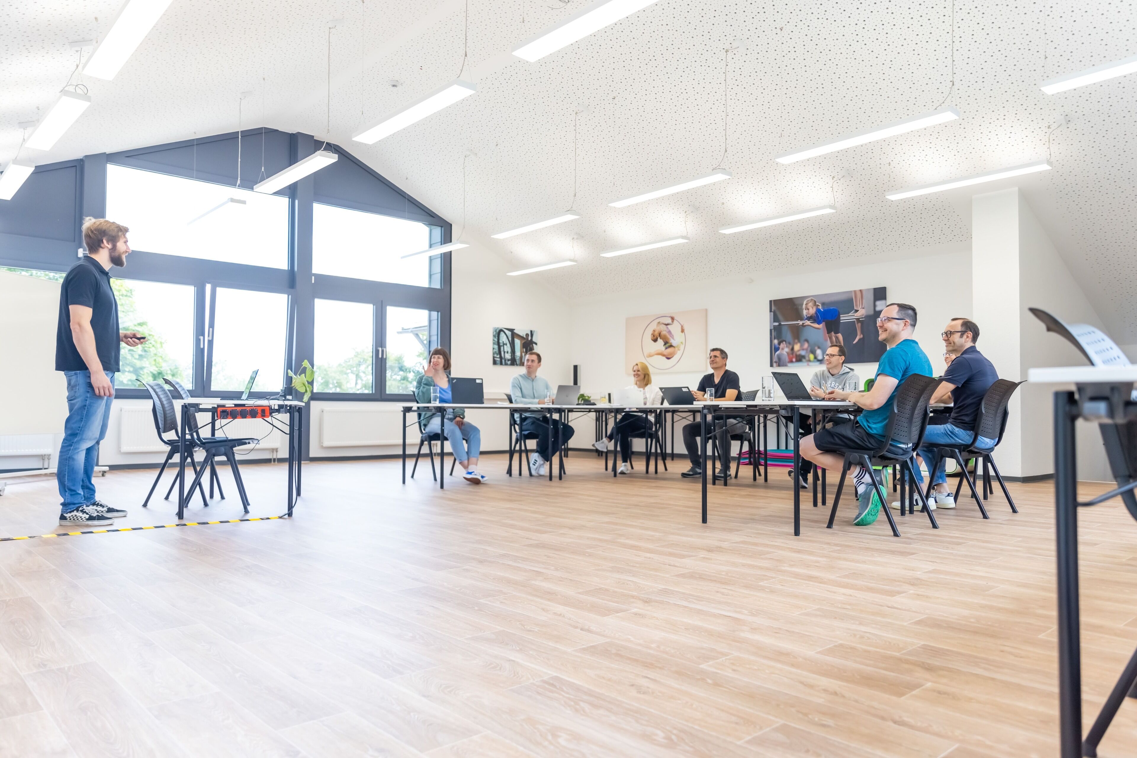 A modern conference room with large windows, a white ceiling, and a group of people seated at a table with laptops.
