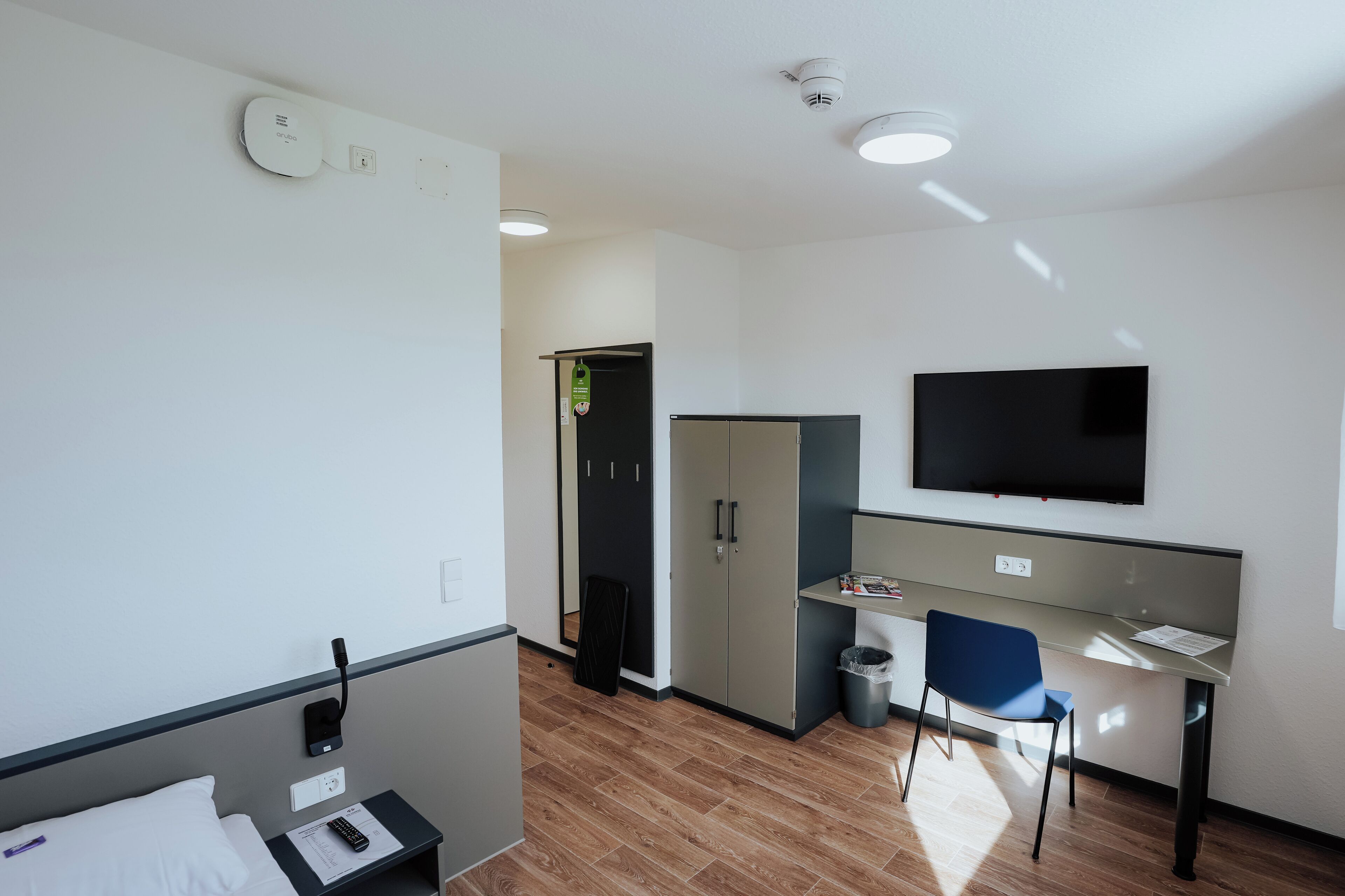 A modern hotel room with a bed, a desk, a chair, a TV, and a wardrobe.
