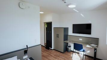 A modern hotel room with a bed, a desk, a chair, a TV, and a wardrobe.