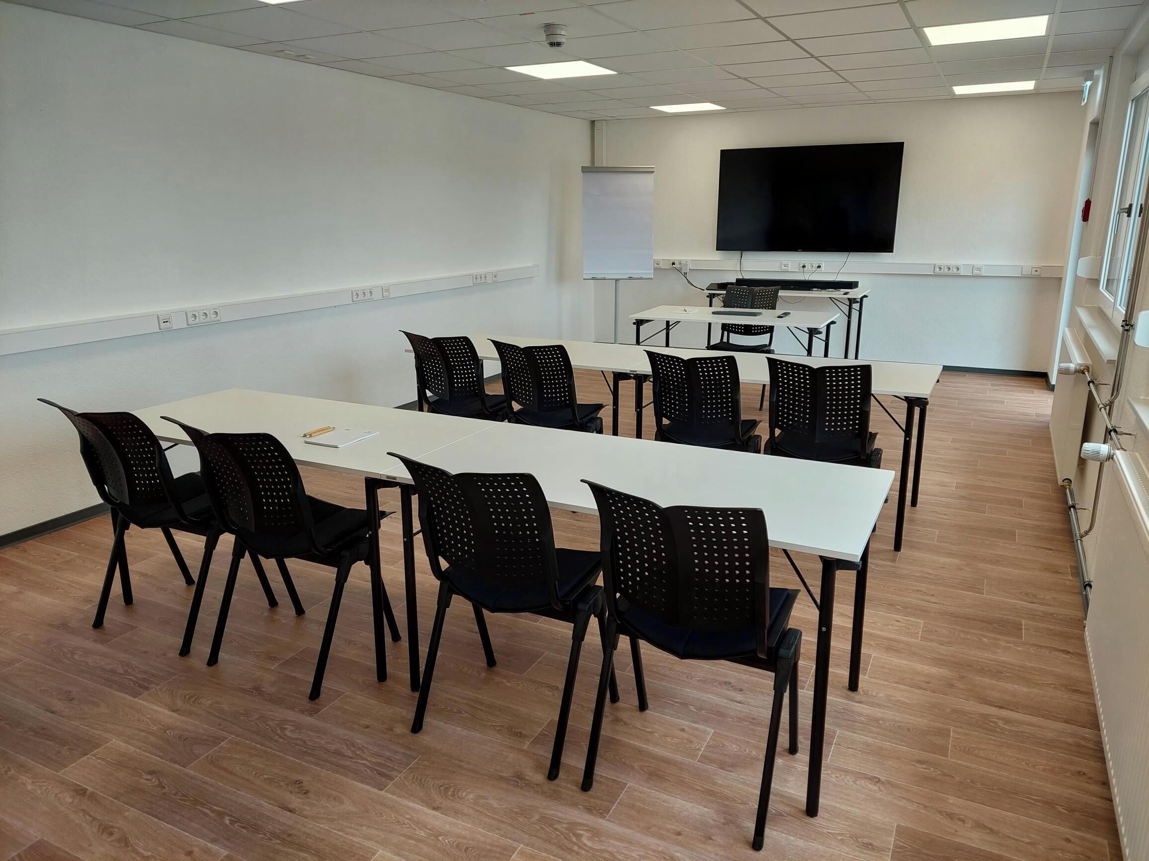 A conference room with a long table, black chairs, a whiteboard, and a TV on the wall.