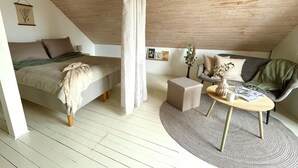 A cozy loft bedroom with a bed, a sofa, a coffee table, and a small table with books and a vase. - The farrier's yard (Hörby)