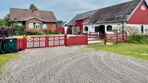 A rural property with a gravel driveway, a red gate, and a barn with a stone wall. - The farrier's yard (Hörby)