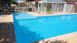 A rectangular swimming pool with a tiled deck, surrounded by a fence and a building with a white exterior. - ‘Salamandre’ Mobile Home with Mountain Views, Shared Pool, and Air Conditioning (Sainte-Croix-du-Verdon)
