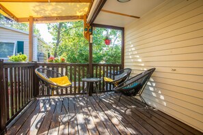 Une terrasse en bois avec deux chaises et une petite table, une plante suspendue, et une vue sur des arbres et une maison.