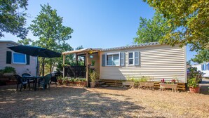 A mobile home with a covered patio, outdoor seating, and potted plants. - ‘Salamandre’ Mobile Home with Mountain Views, Shared Pool, and Air Conditioning (Sainte-Croix-du-Verdon)
