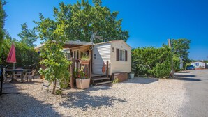 A mobile home with a porch, a table, chairs, and potted plants.
