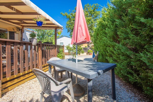 Eine Terrasse im Freien mit Tisch und Stühlen, einem Holzzaun und einem roten Sonnenschirm.