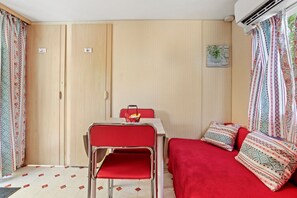 Ein Zimmer mit einem Bett, einem Tisch mit Stühlen, einem roten Sessel, einem kleinen Tisch mit einem Korb und einer Wand-Klimaanlage.