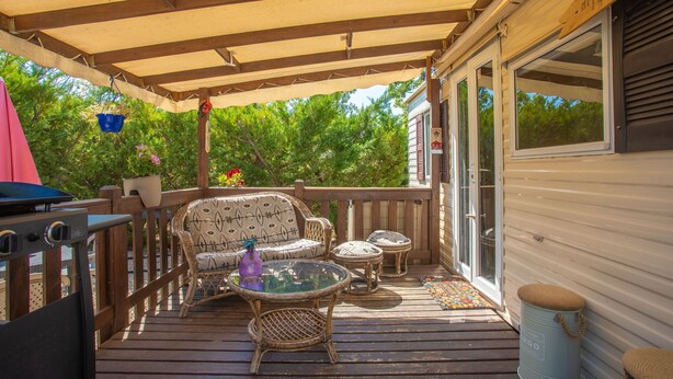A covered deck with wicker furniture, a grill, and a trash can.