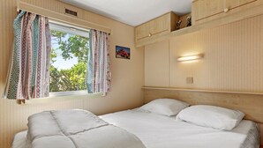 A bedroom with a bed, curtains, a window, a wall-mounted light, and a small picture.