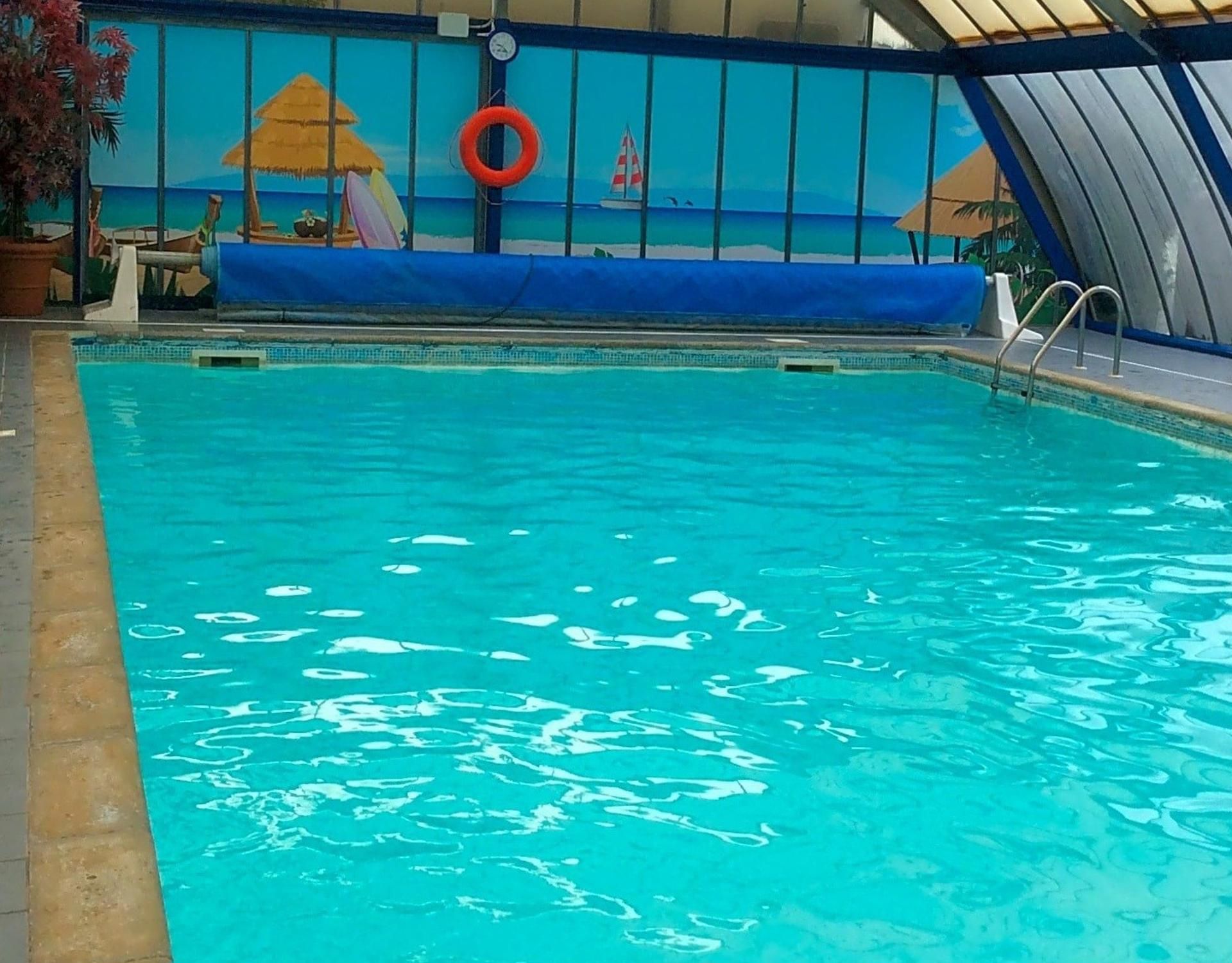 A swimming pool with clear water, a lifebuoy, and a tropical mural in the background.