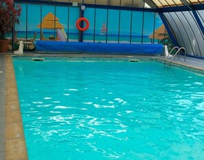 Una piscina con agua cristalina, un flotador salvavidas y un mural tropical al fondo.