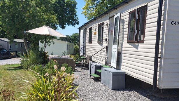 A mobile home with a covered patio, outdoor seating, and a gravel driveway. - Llanarmon-yn-ial Mold 3-bed Caravan, Sleeps 6 (Mold)
