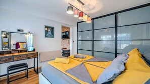 A modern bedroom with a bed, bedside table, mirror, artwork, and a TV.