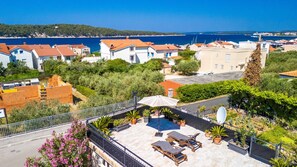 A residential area with a view of the sea, houses with red roofs, and a patio with outdoor furniture.