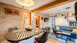 A dining area with a brick wall, a table with chairs, a vase with flowers, and a sofa in the living room.
