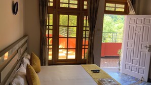 Habitación de hotel con cama, ventana con cortinas, puerta y vista al exterior.