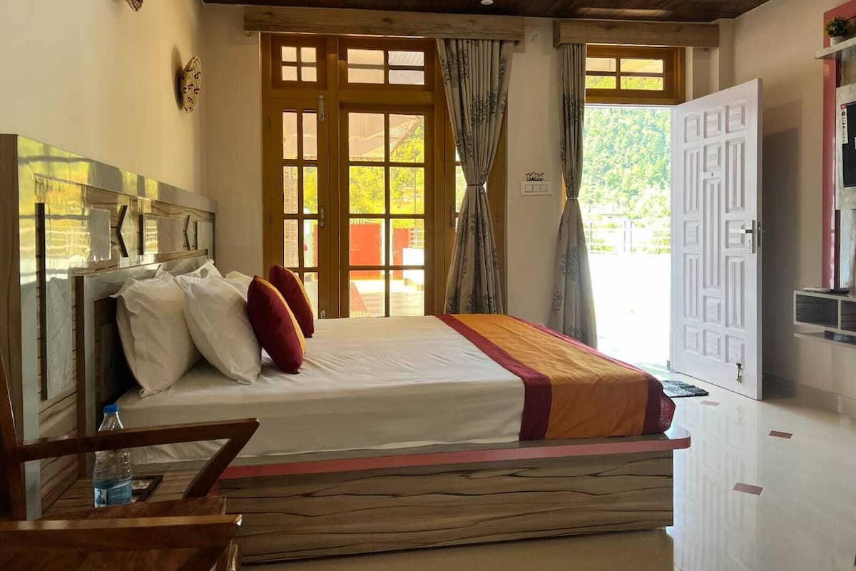Un dormitorio con cabecera de madera, cama con ropa de cama blanca y roja, un banco de madera y un gran ventanal con cortinas.